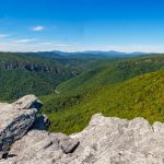 View from Hawksbill Summit overlooking the rugged cliffs and deep forested valleys of Linville Gorge in Pisgah National Forest, with dramatic skies and layers of Blue Ridge Mountains in the distance.