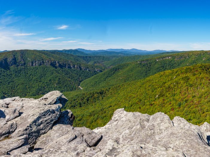 View from Hawksbill Summit overlooking the rugged cliffs and deep forested valleys of Linville Gorge in Pisgah National Forest, with dramatic skies and layers of Blue Ridge Mountains in the distance.